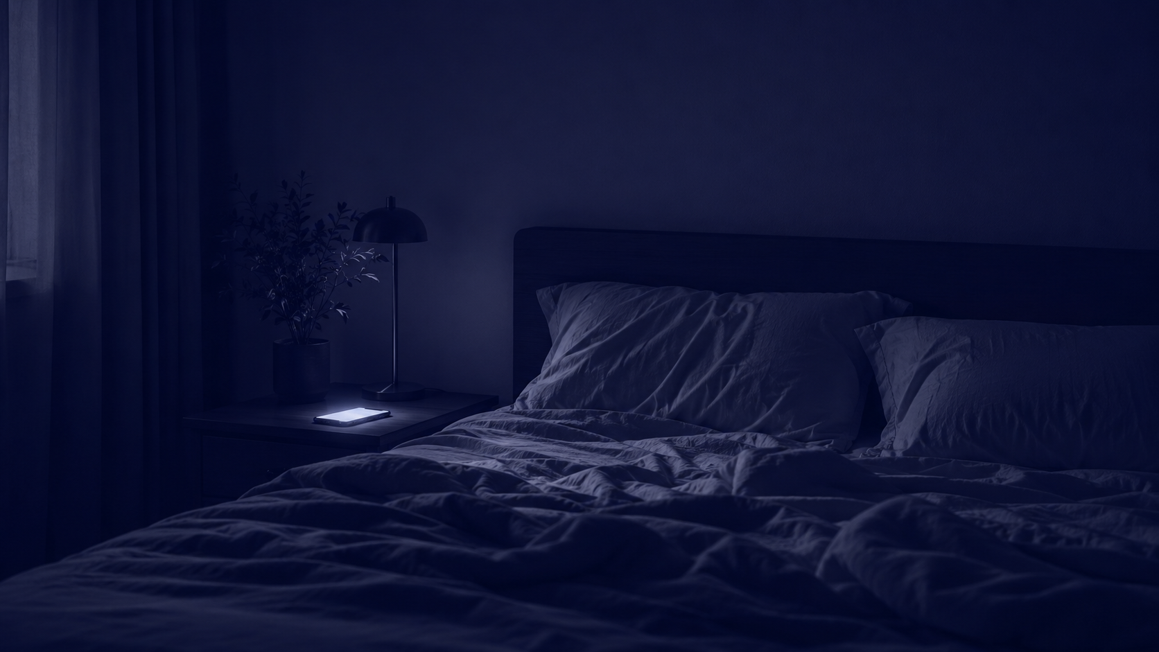 A dark bedroom late at night lit only by a phone glowing on the nightstand.